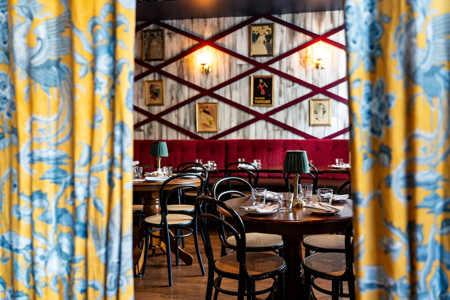 A view through patterned curtains into a cozy, elegant French-style dining room.. 